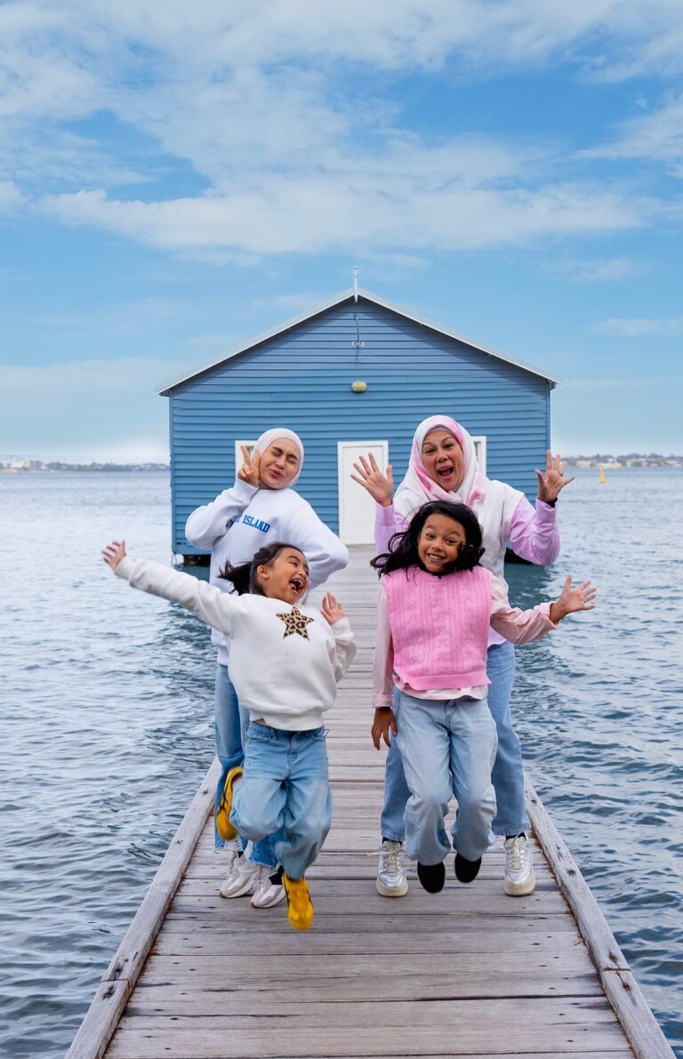 A family jumps delightedly on the pier leading to Crawley Edge Boatshed in Perth, Western Australia.
